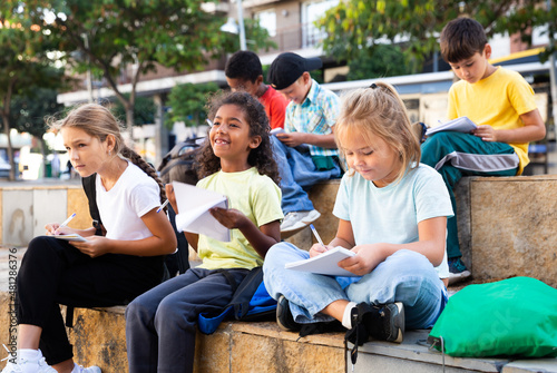 Portrait of multinational group of kids writing in notepads during lesson outdoors