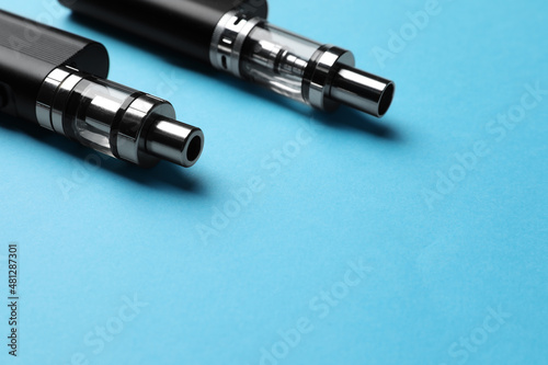 Two electronic cigarettes on light blue background, closeup. Space for text