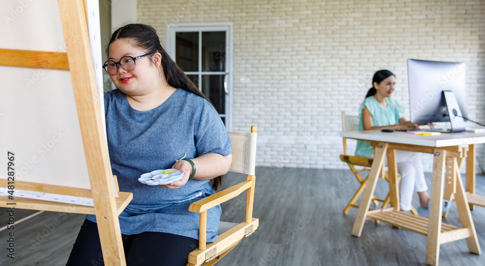 Portrait Asian happy lovely mother sitting crossed arms in front computer encouraging young chubby down syndrome autistic autism little daughter while using paintbrush drawing painting colors. Portrait Asian happy lovely mother sitting crossed arms in front computer encouraging young chubby down syndrome autistic autism little daughter while using paintbrush drawing painting colors.