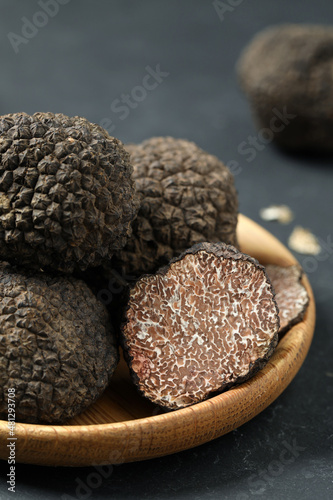 Black truffles in wooden plate on grey table, closeup