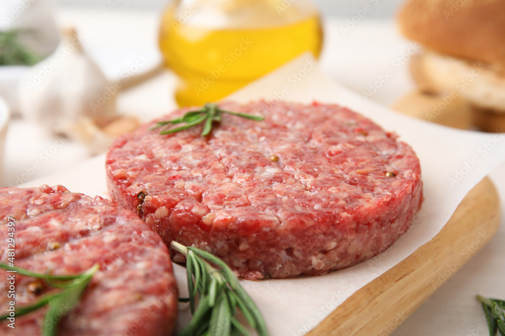 Raw hamburger patties with rosemary on wooden board, closeup