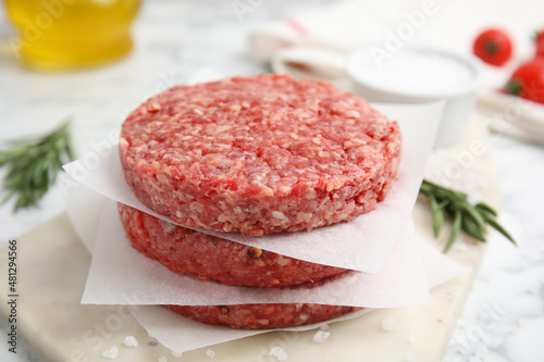 Raw hamburger patties with rosemary and salt on board, closeup
