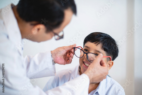 Indian optometrist or optometrist is in white coat helps to get new glasses for boy, child boy in optic store choosing new glasses with optician photo