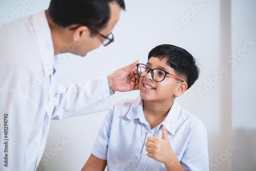 Indian boy try eyeglass frames and thumb up it's perfect for him, optometrist or optometrist helps to get new glasses for boy