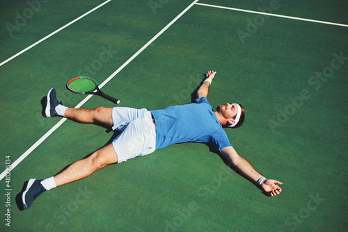 Victory feels so good. Full length shot of a handsome young male tennis player lying down on a tennis court outdoors.
