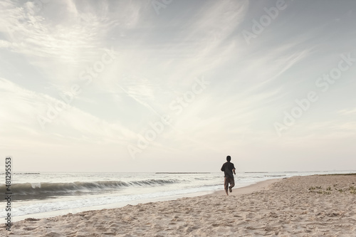 A man jogging on the beach. Sea water waves and sandy beach with copy space in the sky. Exercise and relax with nature in the morning landscape. Ideas for starting a new day. Wellness and motivation.