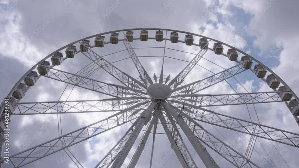 White ferris wheel slowly rotating against the blue sky and clouds background. Slow motion, wide angle shot. White ferris wheel slowly rotating against the blue sky and clouds background. Slow motion, wide angle shot.