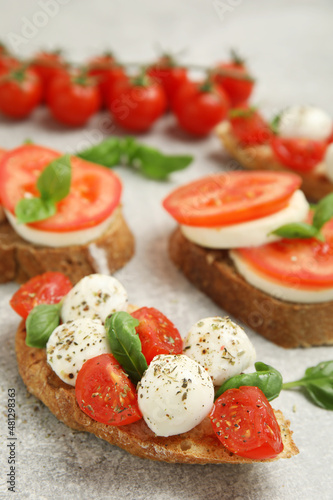 Delicious sandwiches with mozzarella, fresh tomatoes and basil on light grey table