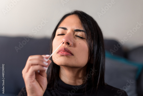 Detail of young woman inserting swab in the nostril at home. Woman doing auto test of covid. photo
