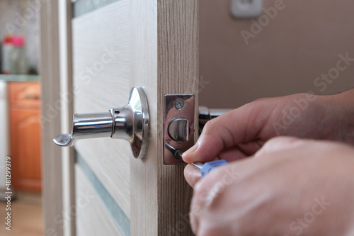 Man repairs lock interior door with screwdriver.