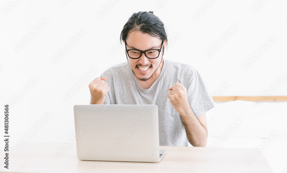 Portrait of Freelancer Asian man sitting on bed at home working on laptop, happy mood, freelancer, free leisure time. Entrepreneur using computer with excited and satisfied, business, success concept.