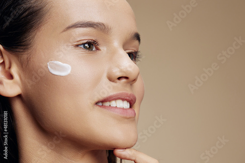 smiling young woman cream on cheek posing cosmetics to clean skin isolated background