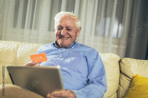 Senior man grandfather shopping online with tablet and credit card at home.