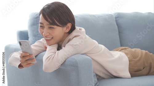 Fotografie ソファでリラックスしながら携帯を触る女性