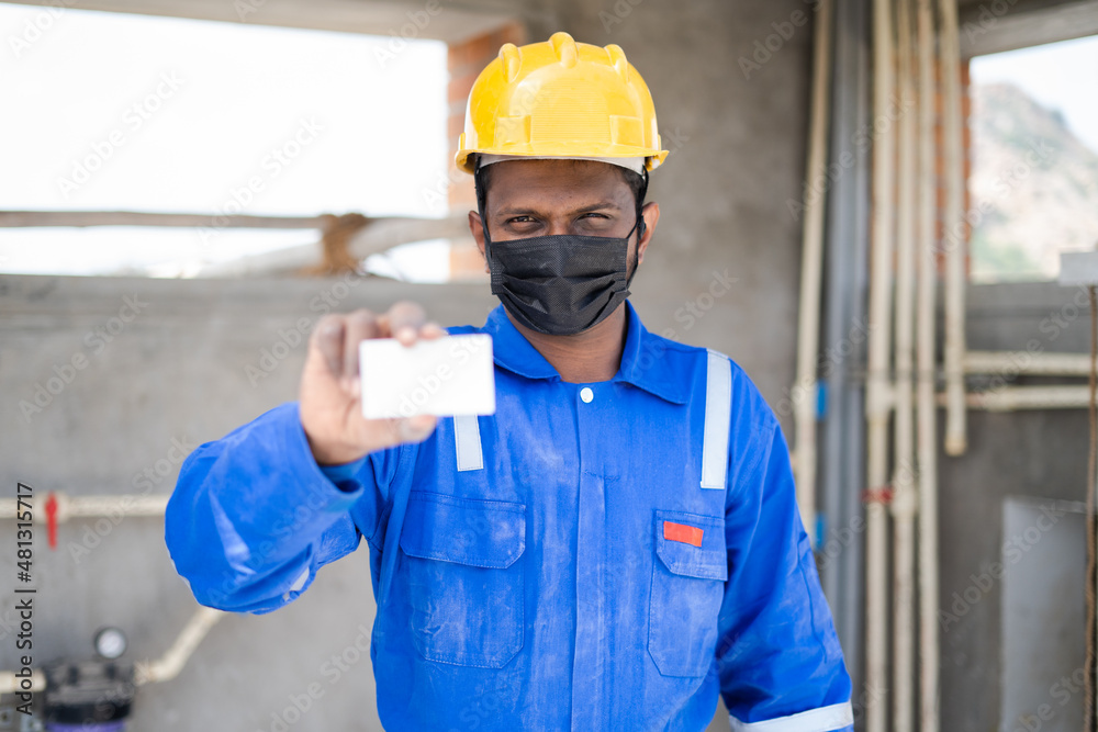 Plumber with medical face mask and safty precautions showing empty card by looking at camera - concept of showing id employee id card, advertisement and promotions. Plumber with medical face mask and safty precautions showing empty card by looking at camera - concept of showing id employee id card, advertisement and promotions.