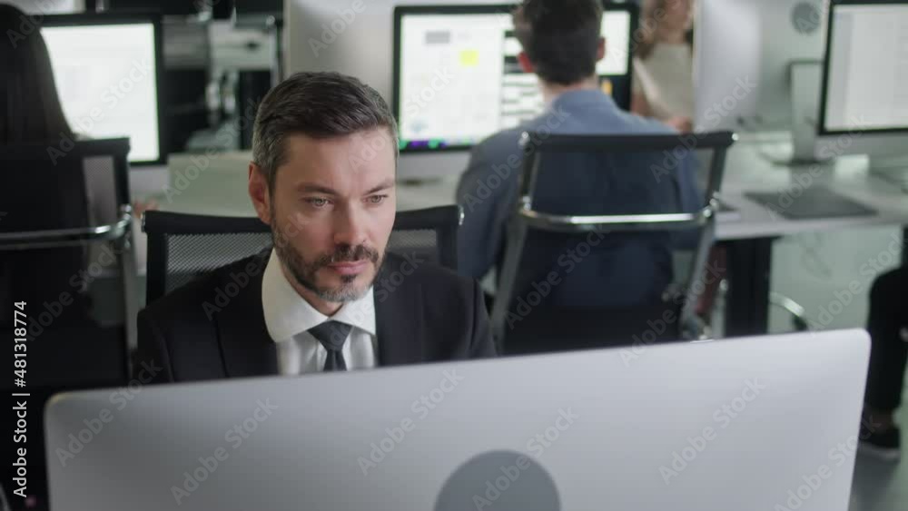 Portrait of Middle-Aged Man in Open Space Office Working on Decktop Computer. Male Professional Typing on PC Keyboard at Office Workplace. Portrait of Serious Business Male Looking at Computer Screen Portrait of Middle-Aged Man in Open Space Office Working on Decktop Computer. Male Professional Typing on PC Keyboard at Office Workplace. Portrait of Serious Business Male Looking at Computer Screen