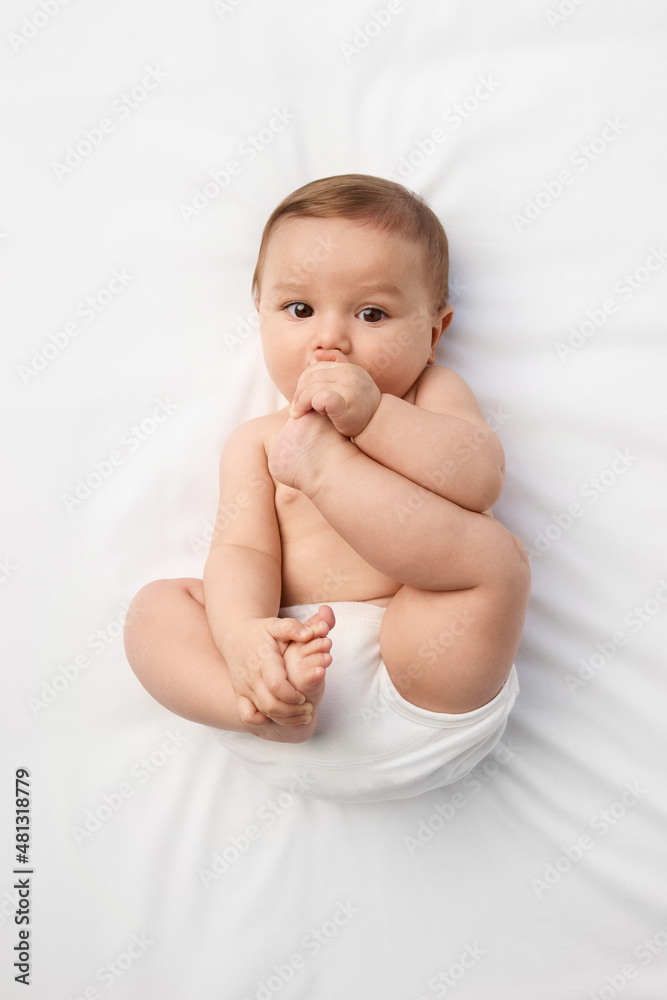 Baby lying on white bed chewing on foot Baby lying on white bed chewing on foot