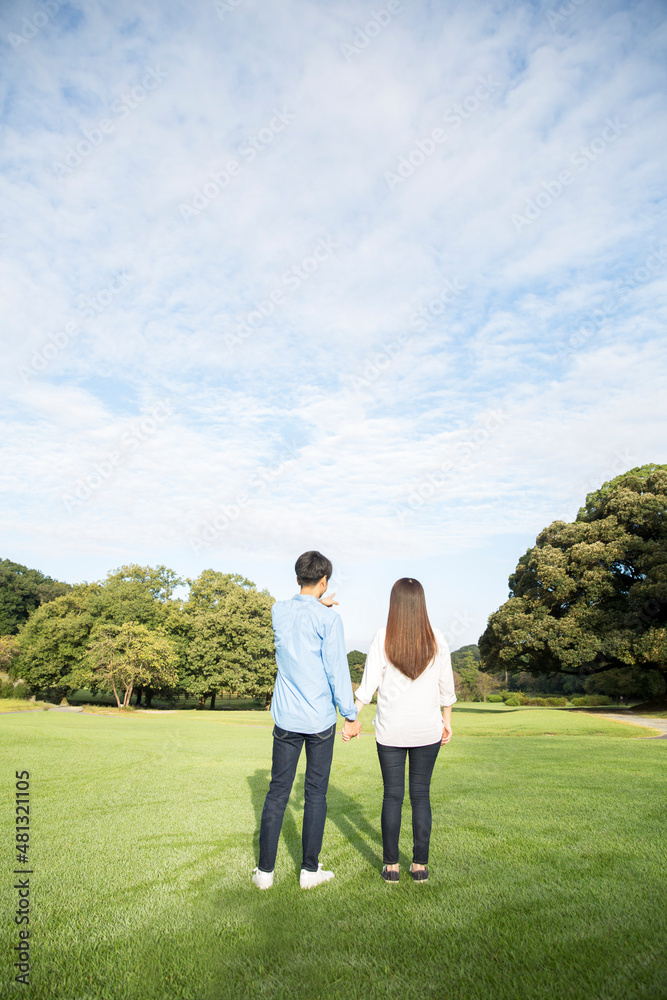 若い日本人カップルの後ろ姿、夏の朝、公園の芝生
