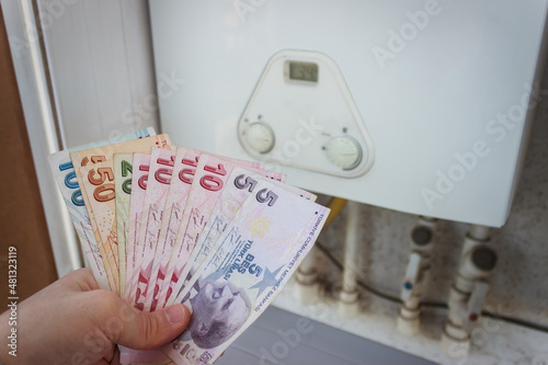 Turkey economic crisis. Turkish lira depreciates. Natural gas and electricity price raise. The man is holding Turkish paper banknotes. Combi boiler at the background. Home economics concept. photo