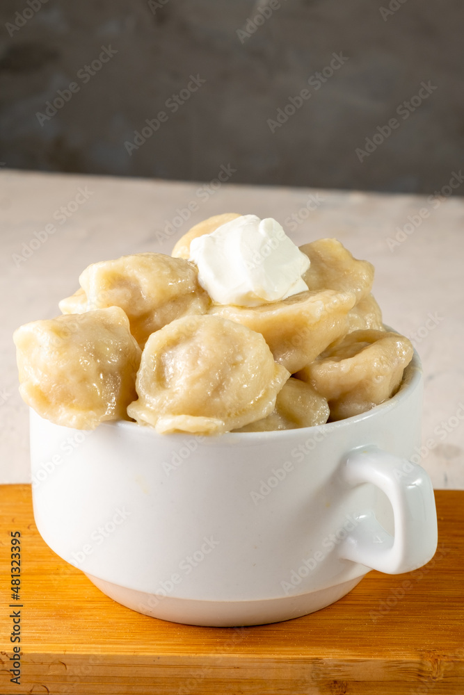 Homemade meat dumplings served in a white bowl with sour cream, close-up. Vertical photo. Homemade meat dumplings served in a white bowl with sour cream, close-up. Vertical photo.