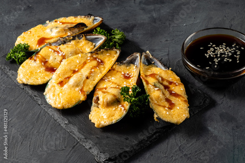Delicious baked mussels in a shell with teriyaki sauce, dark table.