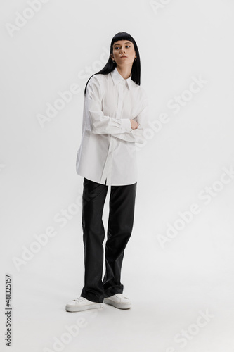 Studio photoshoot of a young brunette woman wearing casual clothing against a white background.  Natural makeup and hairstyle