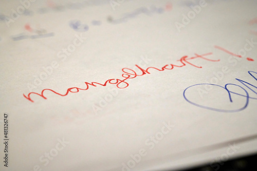 Mit roter Tinte auf einem weißen Blatt geschriebene deutsche Schulnote "mangelhaft" unter einer Klassenarbeit