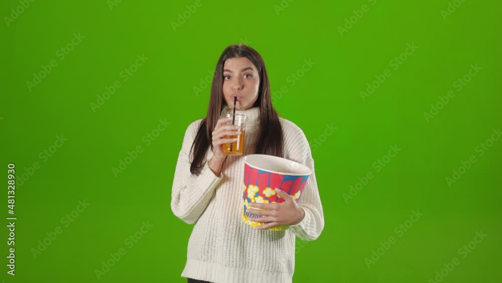 Caucasian woman standing in studio with cup of lemonade and basket of popcorn and feeling confusion while watching some movie. Human emotions and grimace concept. Caucasian woman standing in studio with cup of lemonade and basket of popcorn and feeling confusion while watching some movie. Human emotions and grimace concept.