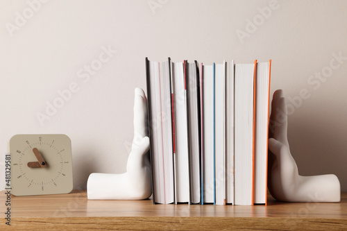 Beautiful hand shaped bookends with books and clock on table near light wall