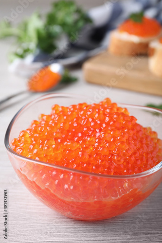 Glass bowl with delicious red caviar on white wooden table, closeup