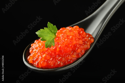 Spoon with delicious red caviar and parsley on black background, closeup