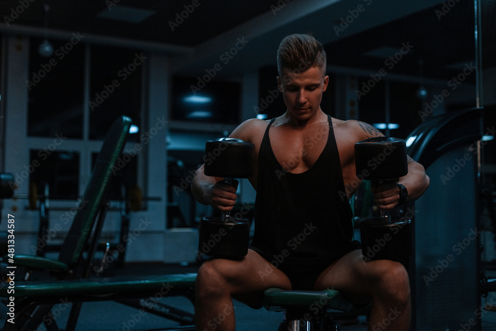 muscular bodybuilder man sits with dumbbells and trains in the gym. Sporty lifestyle muscular bodybuilder man sits with dumbbells and trains in the gym. Sporty lifestyle