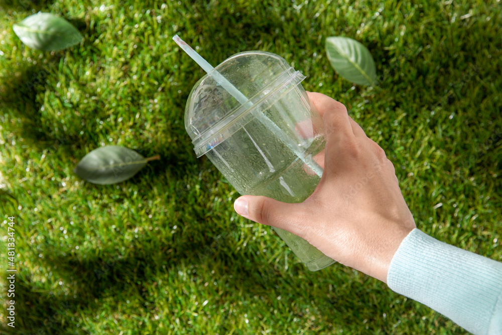 recycling, garbage disposal, environment and ecology concept - close up of hand removing empty used plastic cup from grass