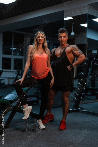 Pretty young slender girl and a sports handsome man with a muscular body with a tattoo train in the gym. Beautiful sports couple and healthy lifestyle