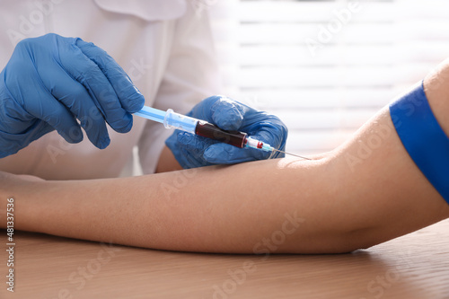 Doctor drawing blood sample of patient with syringe in hospital, closeup photo
