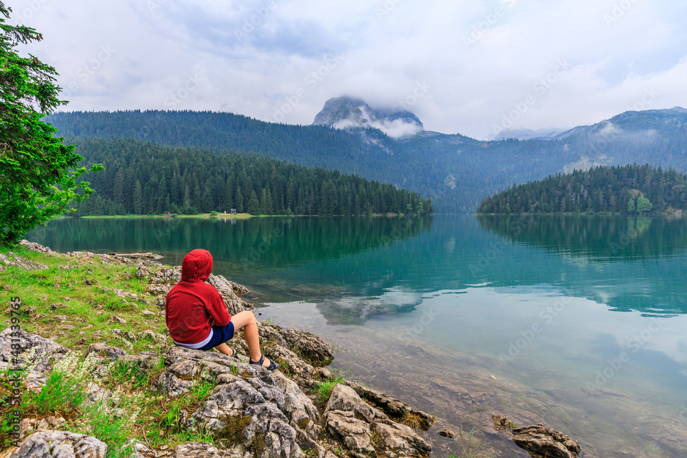Young boy enjoying view of black lake or Crno jezero in Durmitor nature park, Montenegro.