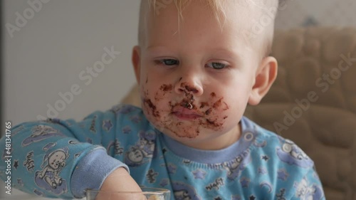 A cute little boy eats chocolate with pleasure smiling and laughing close-up