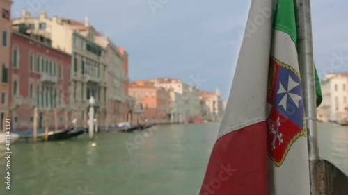 Italian maritime flag waving during boat ride on Grand Canal, Venice, Italy, at day. Medieval buildings in background, selective focus