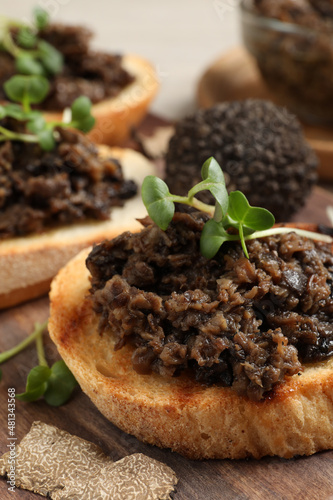 Delicious bruschettas with truffle sauce and microgreens on wooden table, closeup