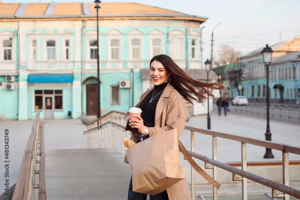 Fototapeta premium Happy woman with waving hair, wearing bige trech coat speinding time outdoors in the city in spring.