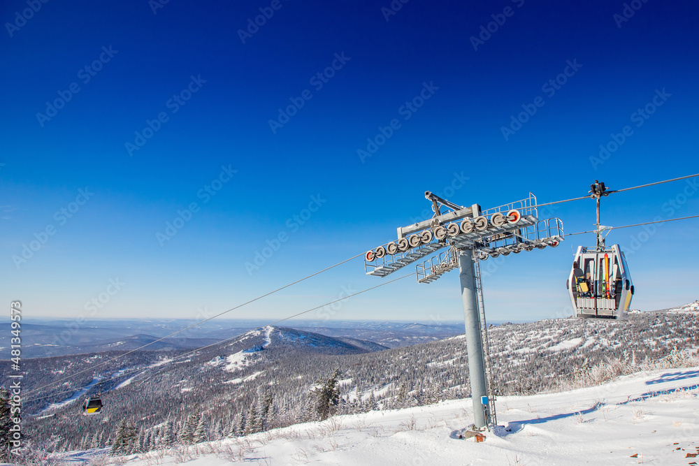 Obraz premium Cabin lift for sheregesh kemerovo ski resort on background of mountains and blue sky, sunny day