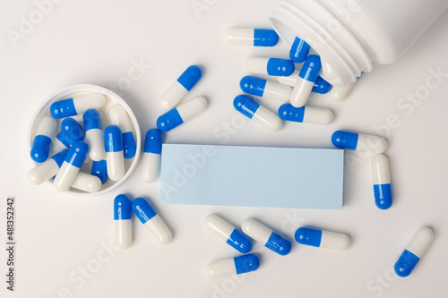 Closeup of a blank blue sticky note and blue-white pills spilling out of pill bottle. Medical concept. Blank space for future important events announcements