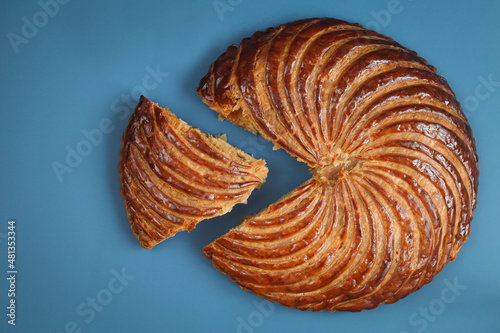 Top view of traditional French galette des rois (king cake) with cut piece, blue background. Cake made with puff pastry and creamy almond filling roll in circles shape. It's usually served on Epiphany