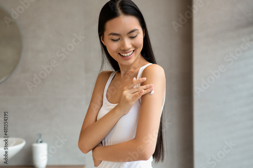 Happy asian woman applying skin butter on her shoulder