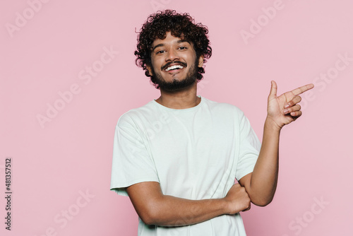 Young middle eastern man smiling and pointing finger aside