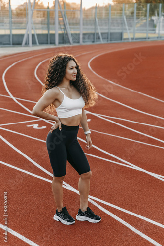 Woman trainer is standing on a running track at morning.