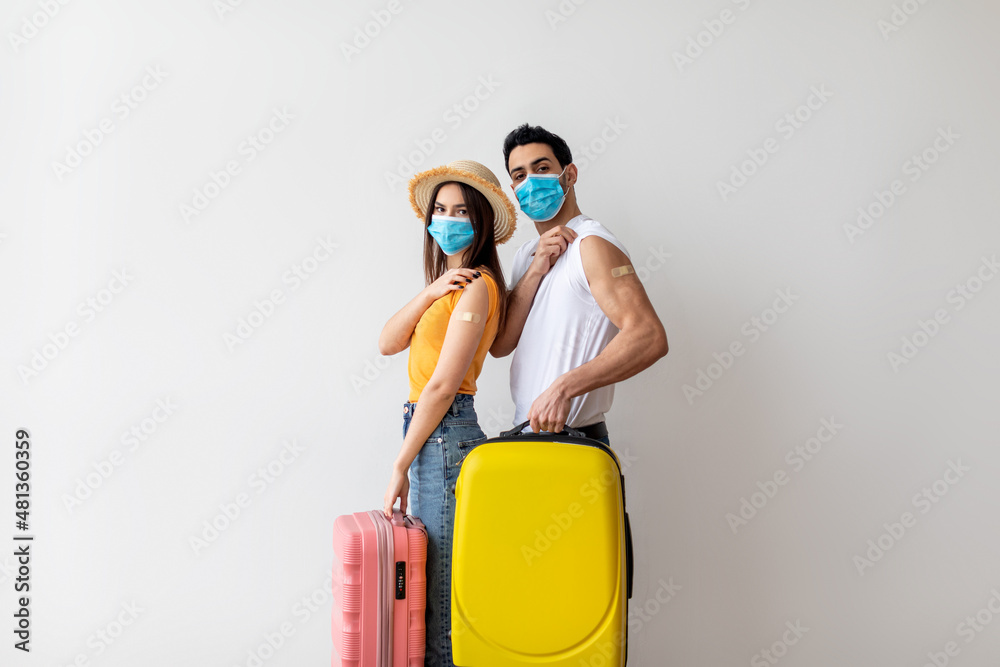 Young couple ready for safe summer holiday journey, holding suitcases and showing arms after receiving covid-19 vaccine - obrazy, fototapety, plakaty 