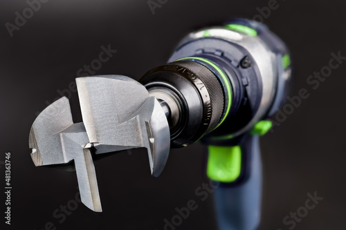 Close-up of steel Forstner bit in cordless drill on a black background. Metal professional cutting tool for boring flat bottomed holes in wood clamped in power drilling machine. Woodworking equipment. photo