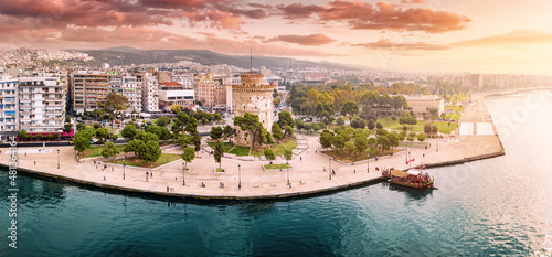 Aerial panoramic view of the main symbol of Thessaloniki city - the White Tower with boat tour ship at the pier. Concept of travel landmarks in Greece and urban development.