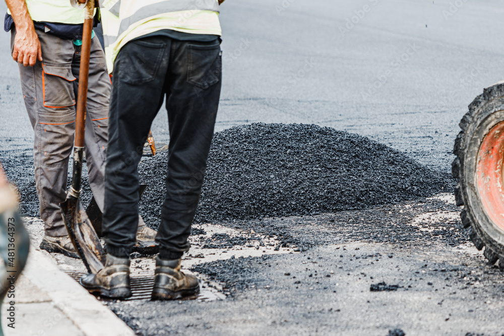 Heavy and dirty manual work on laying fresh asphalt and bitumen on a city street